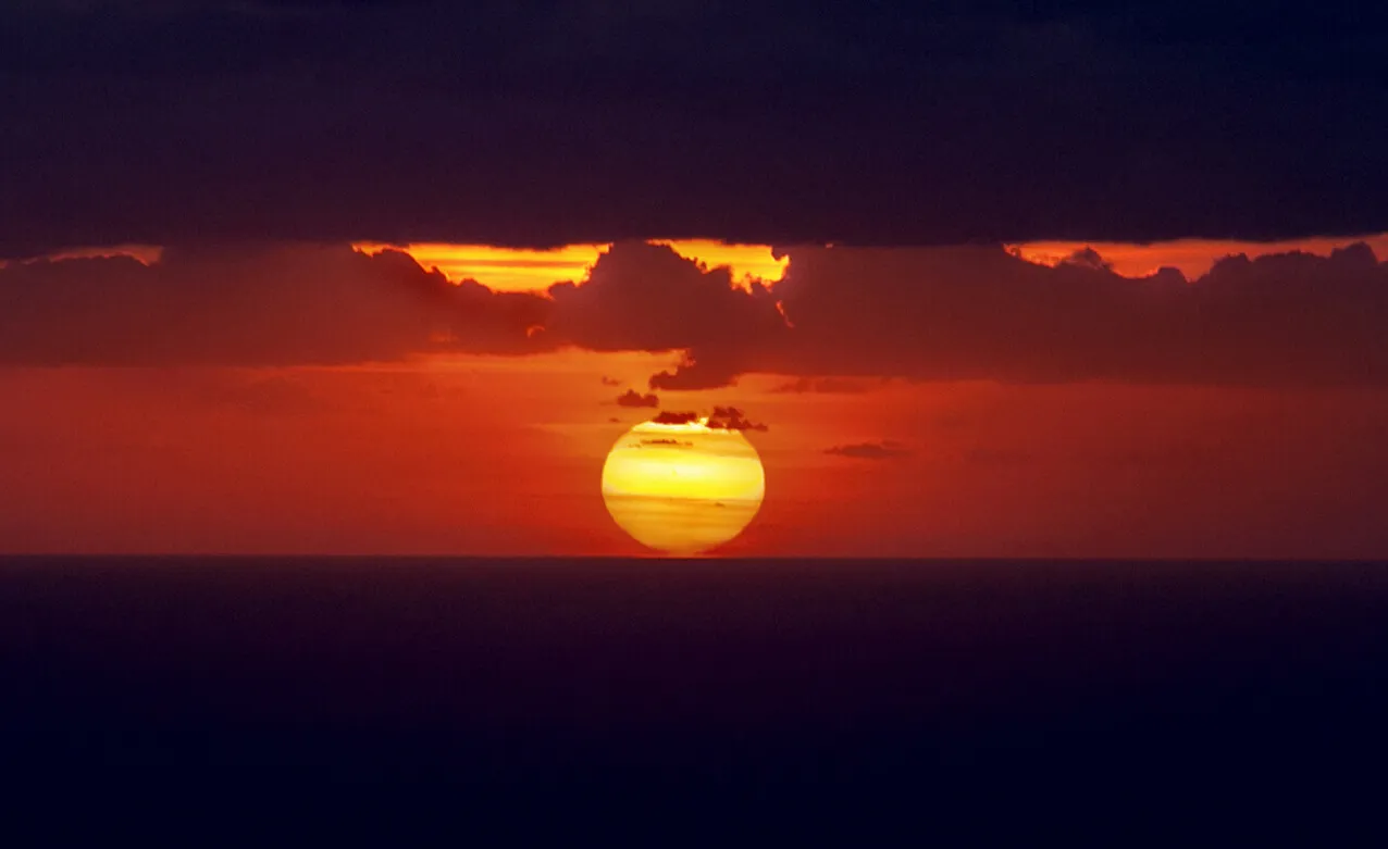 Sole che emerge tra nuvole scure in un cielo arancione.